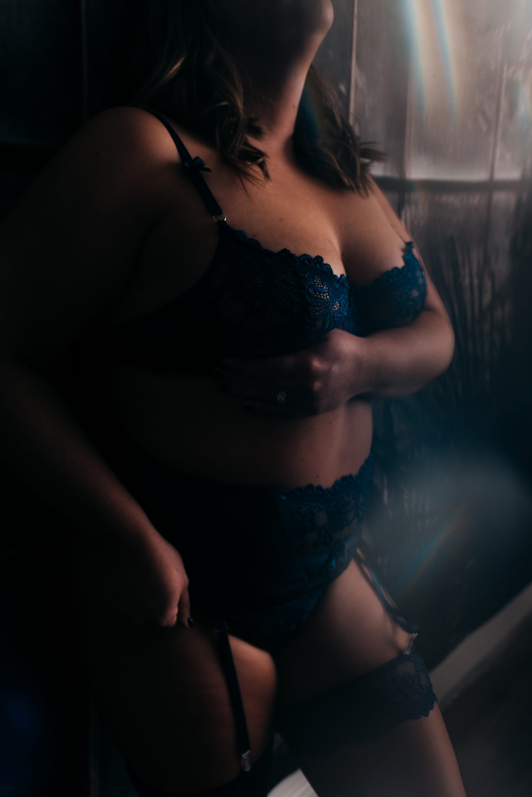 woman wearing blue lingerie during her boudoir experience and standing against a dark wall
