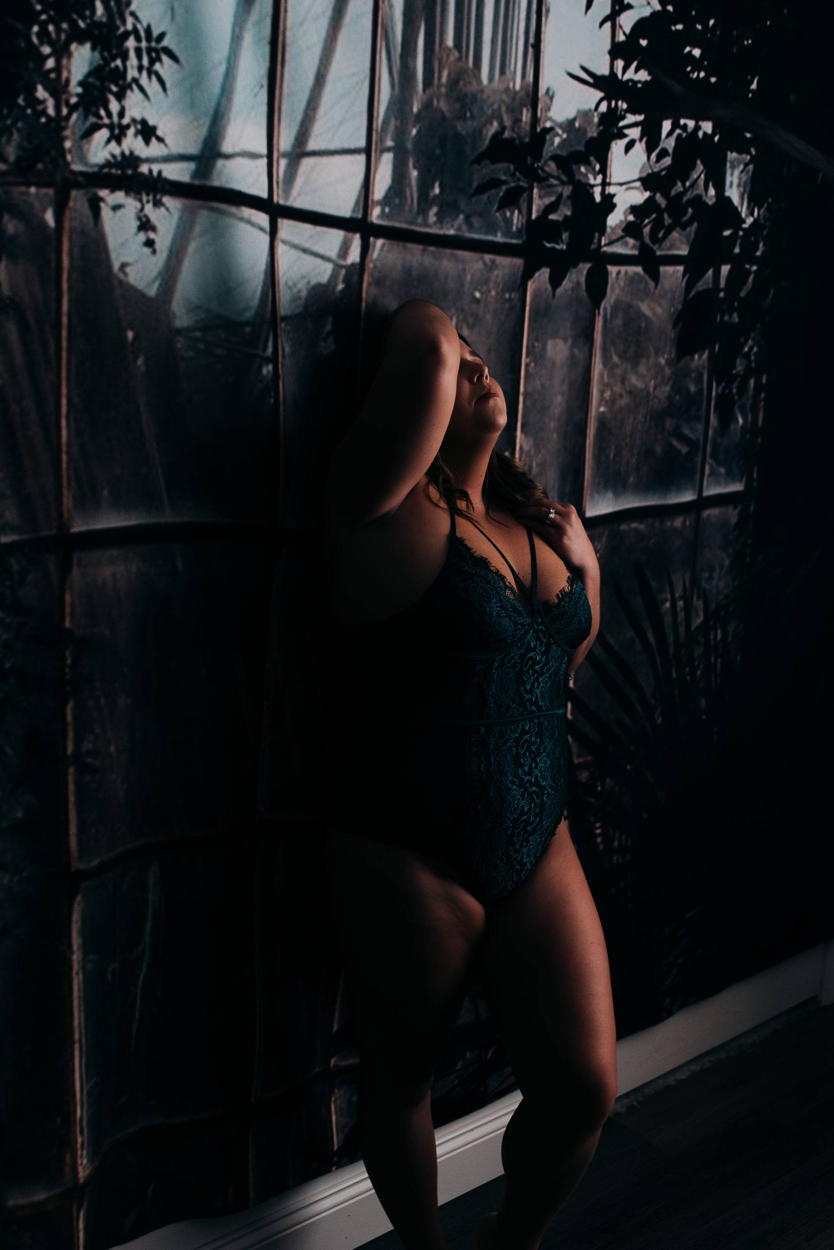 woman wearing green lingerie during her boudoir experience standing against a wall and playing with her hair